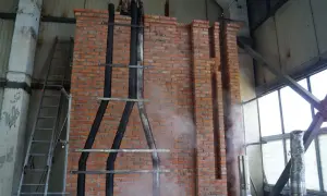 Instalacja wkładu kominowego do starego komina: czarne rury prowadzone po ceglanej ścianie, drabina, para wodna.