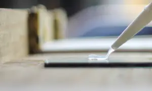 Aplikacja silikonu bez pistoletu. Przezroczysty silikon wypływa z tubki na szklaną powierzchnię, tworząc falisty ślad.