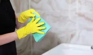 Osoba w żółtych rękawiczkach trzyma zieloną ściereczkę.