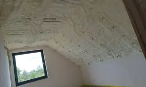 Pianka pur w sprayu izoluje poddasze. Widoczny dach skośny pokryty pianką, okno i ściany.