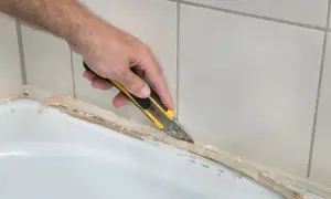 Dłoń z nożem odcina stary silikon z wanny.