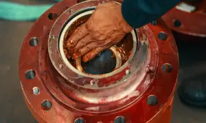 Ręka smaruje łożysko brązowym smarem. To smar silikonowy do czego? Do ochrony i smarowania elementów mechanicznych.