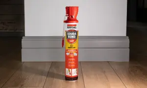 Puszka kleju budowlanego Soudal Easy Bond na drewnianej podłodze, obok szarej listwy przypodłogowej.