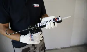 Ręce w białych rękawiczkach trzymają pistolet z tubą silikonu neutralnego białego.