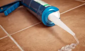 Pistolet do silikonu z wyciśniętym przezroczystym silikonem na brązowych płytkach. Zastanawiasz się, jak długo schnie silikon uniwersalny?