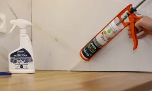 Aplikacja silikonu do blatu kuchennego. Pistolet z kartuszem Bostik Perfect Seal Kuchnia aplikuje masę uszczelniającą. Obok stoi butelka preparatu do wygładzania fug.