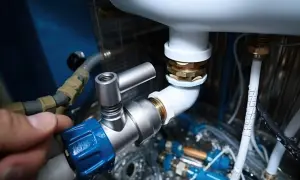 Dłoń dokręca zawór przy białej rurze PCV, elementach instalacji wodnej.
