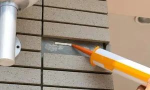 Aplikator z pomarańczową dyszą aplikuje biały silikon w szczelinę między płytkami. Dowiedz się, jak wyrównać silikon dla idealnego efektu.
