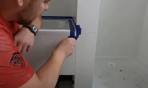 Mężczyzna w czerwonej koszulce przygotowuje się do tego, jak silikonować narożniki, oklejając je taśmą.