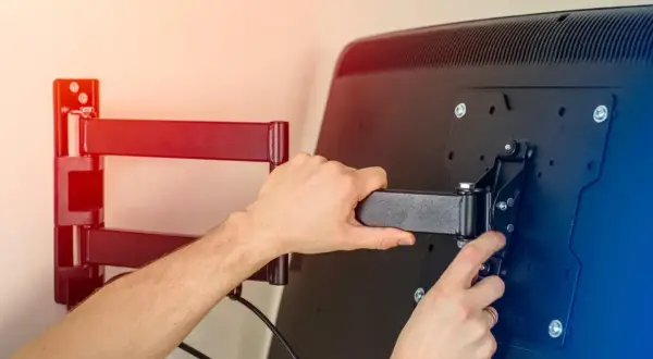 Montaż telewizora na ścianie. Ręce przykręcają uchwyt do ekranu, przygotowując mocowanie telewizora na ścianie.