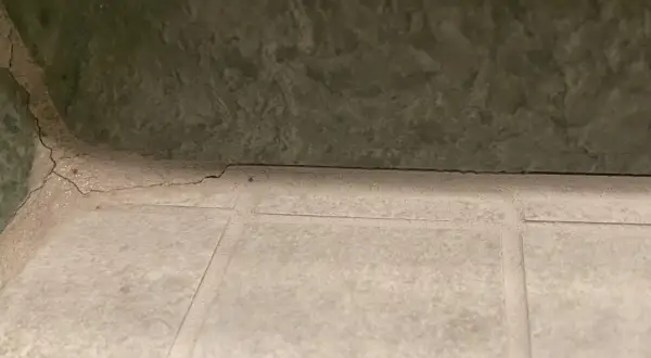 Pęknięta, biała masa między płytkami sugeruje, że szukamy co zamiast fugi. Zielona ściana nad nią.