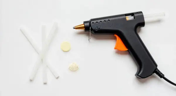Czarny pistolet do kleju na gorąco z pomarańczowym spustem i kilkoma pałeczkami kleju obok. Dowiedz się, jak włożyć klej do pistoletu.
