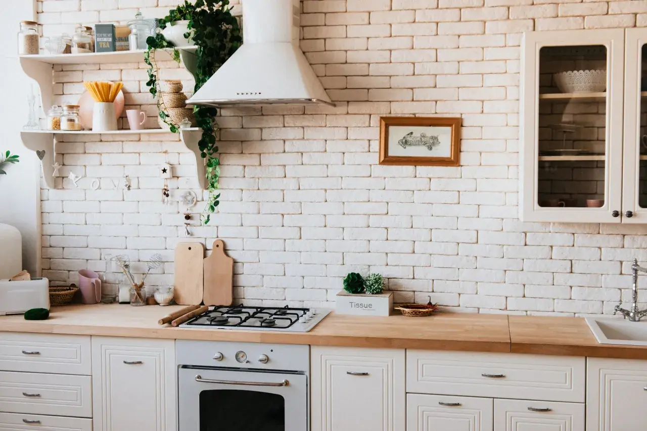 Inspiracja do tego, jak zrobić blat kuchenny z płytek ceramicznych. Jasna kuchnia z drewnianym blatem, białą cegłą i roślinami.