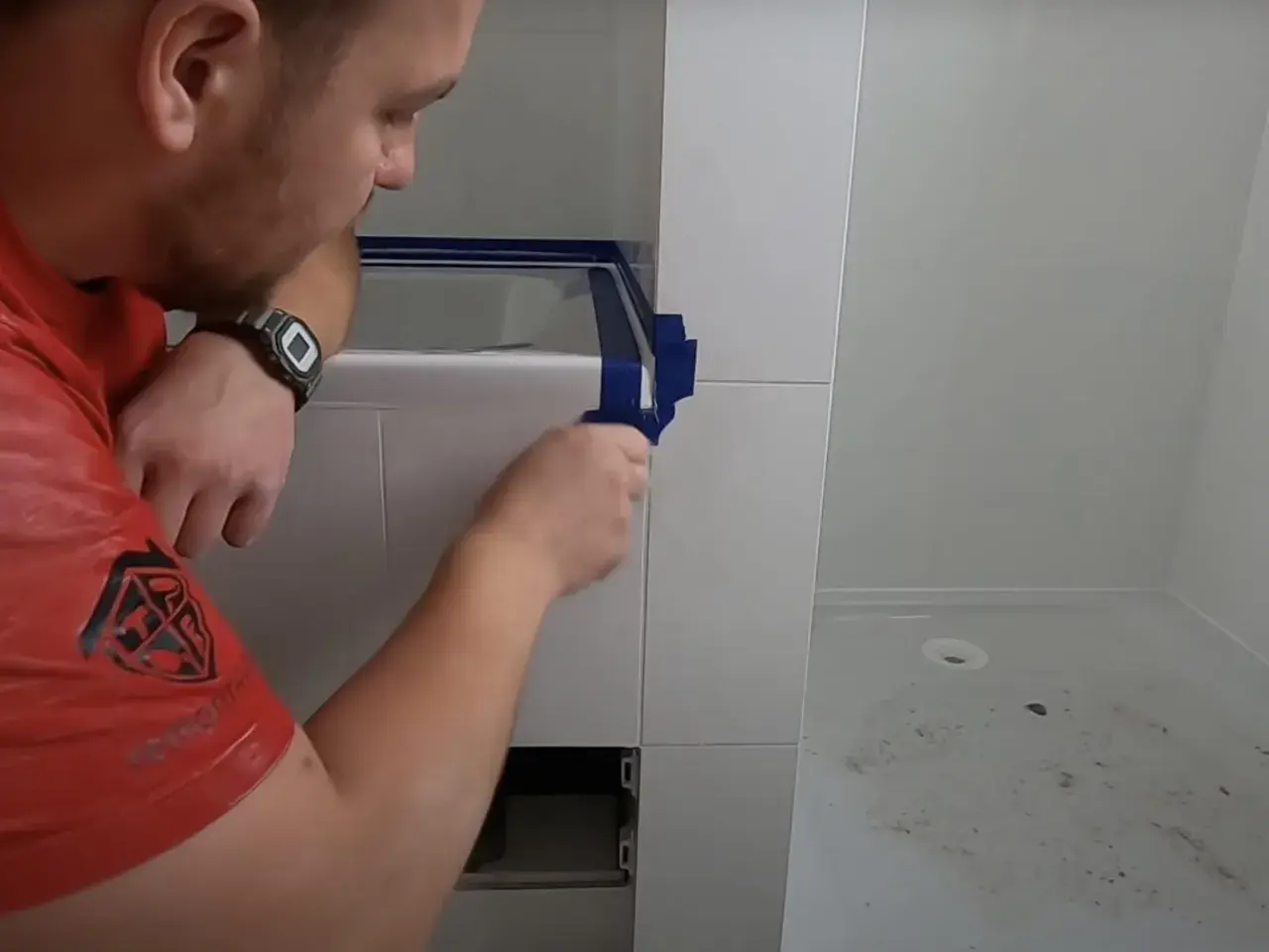 Mężczyzna w czerwonej koszulce przygotowuje się do tego, jak silikonować narożniki, oklejając je taśmą.