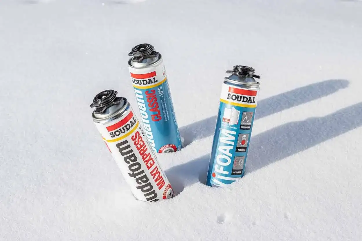 Trzy puszki pianki montażowej zimowej Soudal w śniegu. Jedna to pianka "Maxi Express", druga "Classic", a trzecia "Foam".