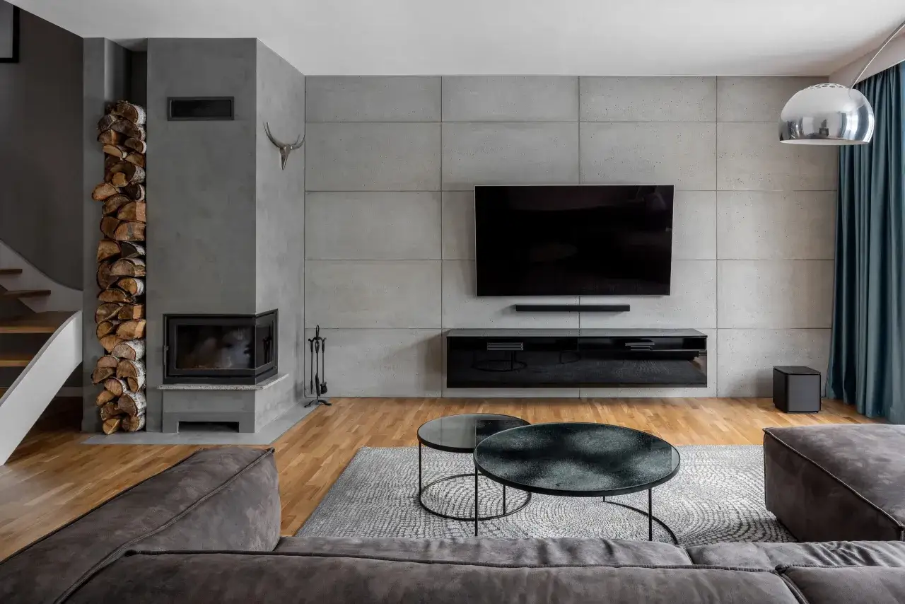 Nowoczesny salon z betonową ścianą, kominkiem i telewizorem. Beton dekoracyjny na ścianie nadaje wnętrzu industrialny charakter.