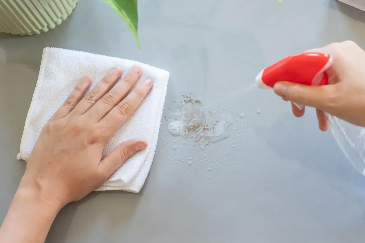 Ręka z białą ściereczką usuwa klej po taśmie, spryskany płynem ze sprayu.
