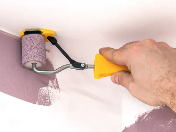 Ręka trzyma żółty uchwyt wałka do malowania narożników. Dowiedz się, jak przygotować nowy wałek do malowania, by uzyskać idealne wykończenie.