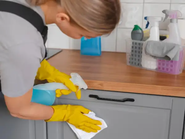 Kobieta w żółtych rękawiczkach czyści szarą szafkę kuchenną, pokazując jak odtłuścić meble kuchenne.