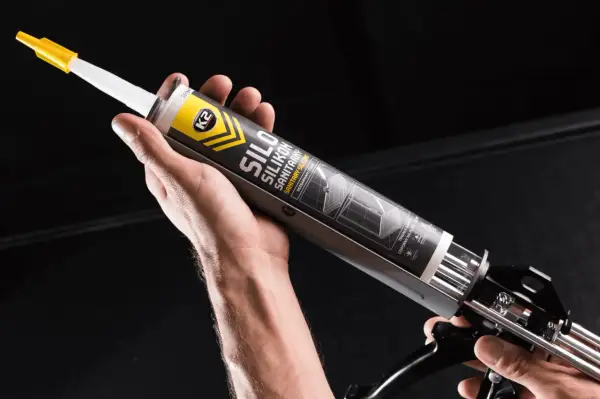 Dłoń trzyma pistolet z tubą silikonu sanitarnego K2. Czy można kłaść silikon na nowy silikon? Ten produkt pomoże Ci to sprawdzić.