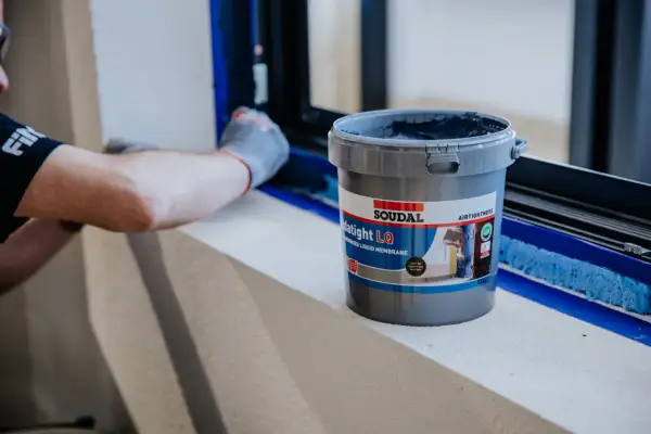 Pracownik nakłada na ramę okna membranę Soudal Datight LQ. Karta charakterystyki pianka montażowa Soudal jest kluczowa dla prawidłowego montażu.
